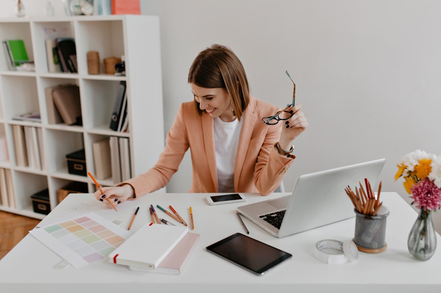 Joyful woman in peach-colored jacket with smile examines documents while sitting in her comfortable bright office