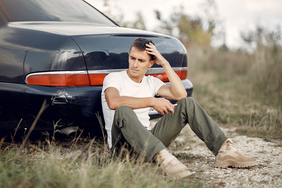 Man near the car. Guy sitting on the ground.